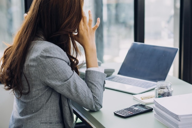 Jeune femme d'affaires assise au bureau à table et utilisant un smartphone Sur le bureau se trouve un ordinateur portable et une tablette sur des graphiques et des graphiques à l'écran Femme analysant des données Étudiant apprenant en ligne