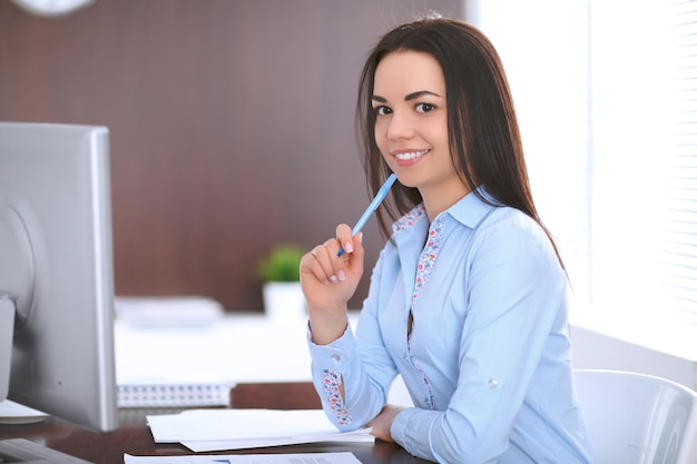 Jeune femme d'affaires assise et écrivant à la table au bureau