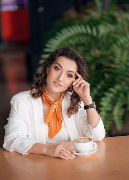 Jeune femme d'affaires assise à une table dans un café buvant du café, elle porte une veste blanche