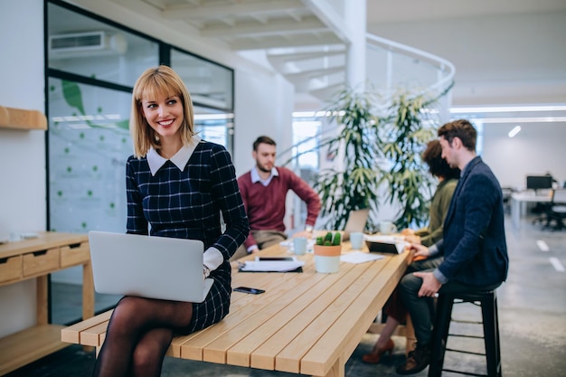 Jeune femme d'affaires assise sur la table tenant un ordinateur portable