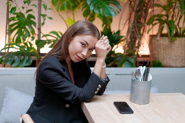 Jeune femme d'affaires attrayante assise à une table dans un café dans un costume noir