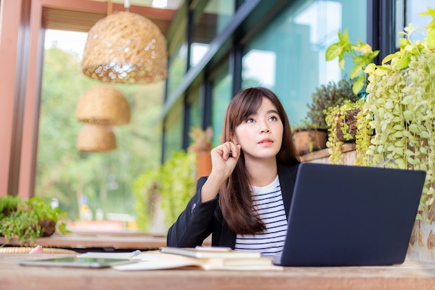 Jeune femme d'affaires attrayante dans son costume décontracté travaillant sur son ordinateur au patio extérieur de son bureau, travaillant mobile ou jeune entrepreneur concept