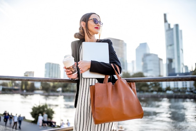 Jeune femme d'affaires ayant une pause-café à l'extérieur assise sur le pont dans la ville de Francfort pendant le coucher du soleil