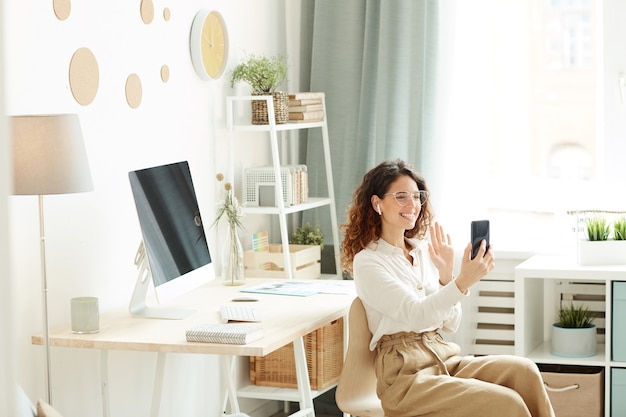 Jeune femme d'affaires ayant une vidéoconférence avec ses collègues à l'aide de smartphone tout en restant à la maison