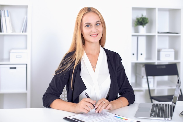 Jeune femme d'affaires blonde avec ordinateur portable au bureau.