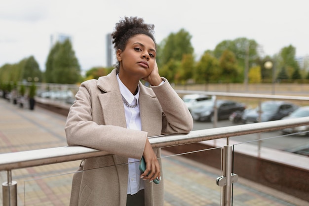 Jeune femme d'affaires bouclée américaine regardant pensivement la caméra dans la rue