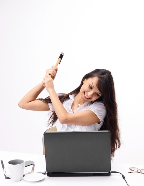 Jeune femme d'affaires brisant un ordinateur portable assis derrière un bureau