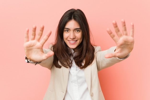 Jeune femme d'affaires brune contre un mur rose montrant le numéro dix avec les mains.