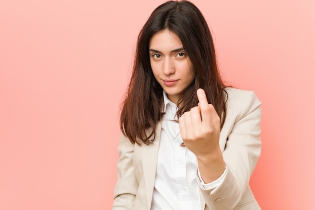 Jeune femme d'affaires brune contre-pointes pointant du doigt vers vous comme si vous invitiez à vous en approcher.