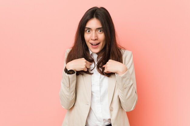 Jeune femme d'affaires brune contre un rose surpris pointant avec le doigt, souriant largement.