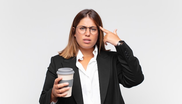 Jeune femme d'affaires avec un café confus et perplexe, montrant que vous êtes fou, fou ou hors de votre esprit