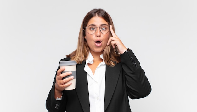 Jeune femme d'affaires avec un café à la surprise, la bouche ouverte, choquée, réalisant une nouvelle pensée, idée ou concept