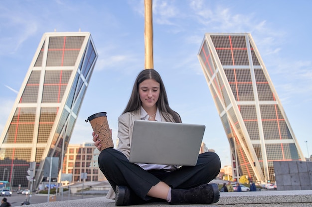 Jeune femme d'affaires caucasienne assise devant son ordinateur portable à l'extérieur d'un immeuble de bureaux