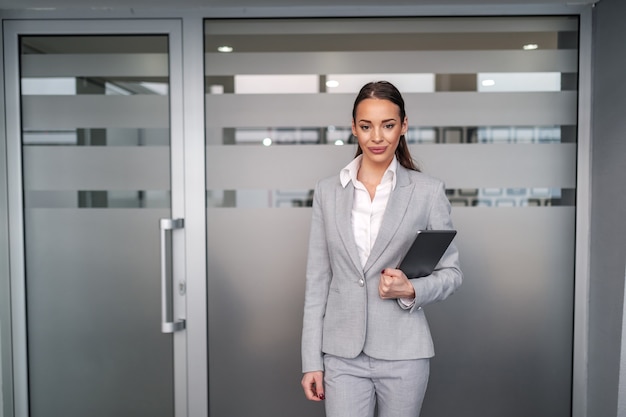 Jeune femme d'affaires caucasienne attrayante en tenue de soirée debout devant la salle de conférence et tenant la tablette dans les mains. Concept d'entreprise.