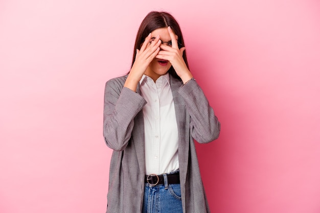 Jeune femme d'affaires caucasienne sur un clin de œil rose à travers les doigts effrayés et nerveux.