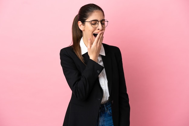 Jeune femme d'affaires caucasienne isolée sur fond rose bâillant et couvrant la bouche grande ouverte avec la main