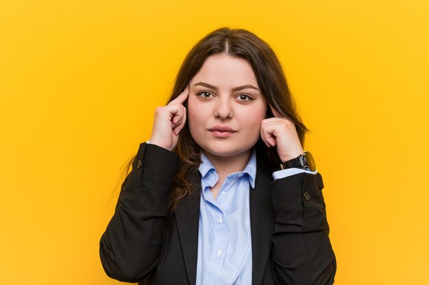 Jeune femme d'affaires caucasienne de taille plus concentrée sur une tâche, le tenant des index pointés vers la tête.