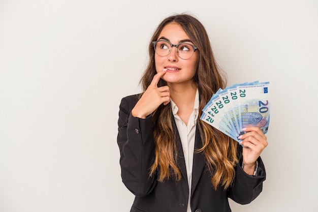 Jeune femme d'affaires caucasienne tenant des billets isolés sur fond blanc détendue en pensant à quelque chose en regardant un espace de copie.