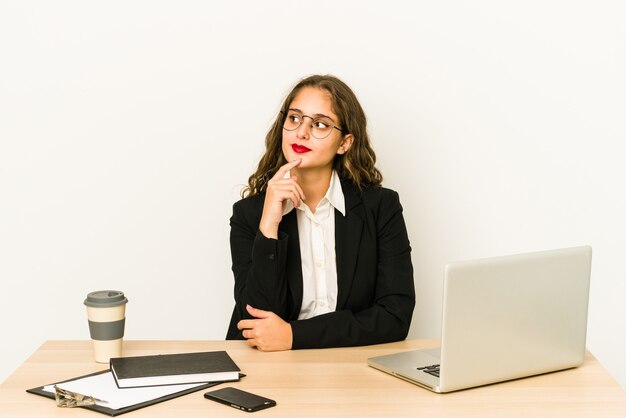 Jeune femme d'affaires caucasienne travaillant sur son bureau isolé à la recherche sur le côté avec une expression douteuse et sceptique.