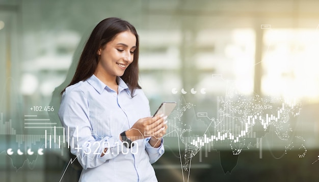 Une jeune femme d'affaires en chemise bleu clair utilise son smartphone avec des graphiques financiers numériques