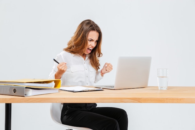 Jeune femme d'affaires en colère utilisant un ordinateur portable et criant sur fond blanc