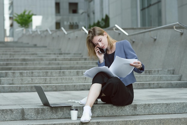 Jeune femme d'affaires concentrée lisant les documents assis dans les escaliers près du centre d'affaires