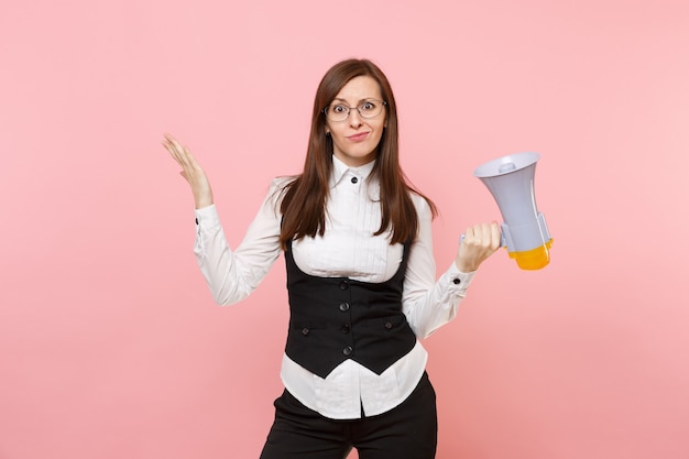 Jeune femme d'affaires concernée en costume noir et lunettes tenant un mégaphone et écartant les mains isolées sur fond rose. Dame patronne. Concept de richesse de carrière de réalisation. Copiez l'espace pour la publicité.