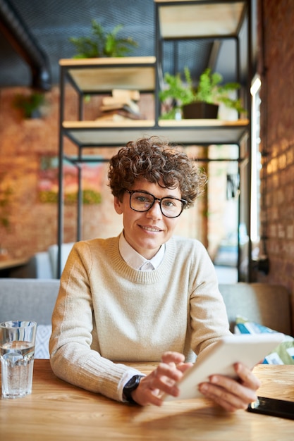 Jeune femme d'affaires confiante dans le défilement décontracté intelligent dans le pavé tactile tout en réseautant par table au café