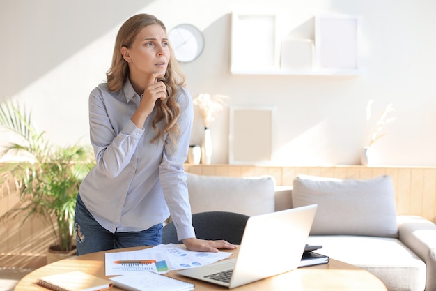 Jeune femme d'affaires confiante avec un sourire amical, debout derrière son bureau dans un bureau à domicile.