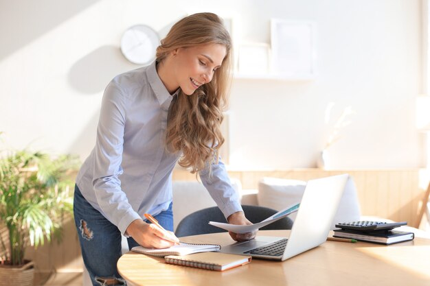 Jeune femme d'affaires confiante avec un sourire amical, debout derrière son bureau dans un bureau à domicile.