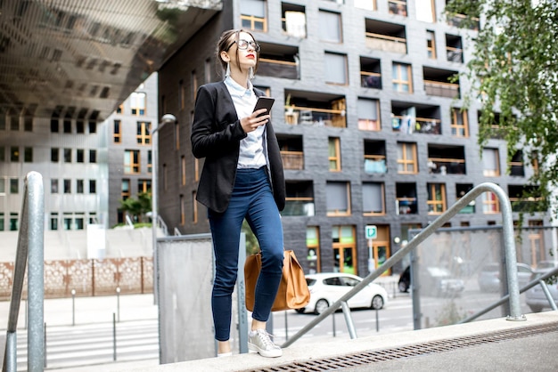 Jeune femme d'affaires en costume courant avec sac et téléphone dans le quartier résidentiel moderne