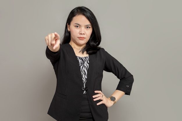 Jeune femme d'affaires en costume noir pointe vers l'avant avec une expression faciale sérieuse