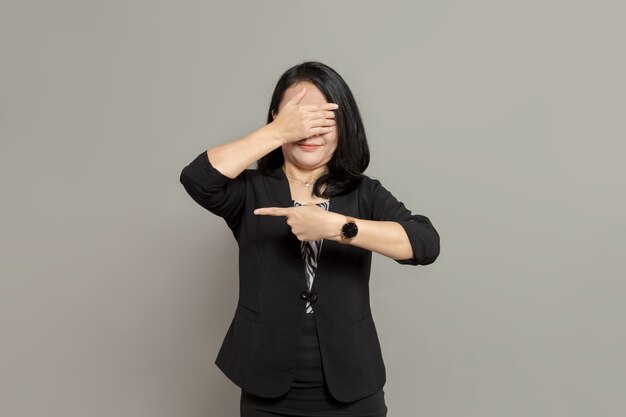 Une jeune femme d'affaires en costume noir pointe vers la gauche tout en se couvrant les yeux avec ses mains