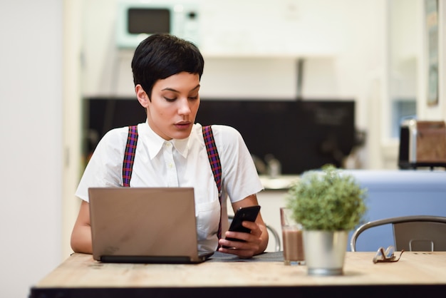 Jeune femme d'affaires avec une coupe de cheveux très courte en regardant son smartphone à la maison.