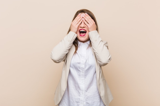 Jeune femme d'affaires couvre les yeux avec les mains, un large sourire attend une surprise.