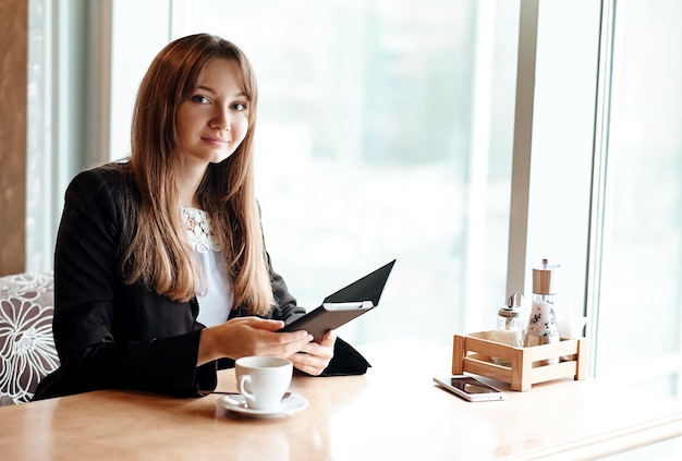 Jeune femme d'affaires dans un café lisant un ebook et buvant du café