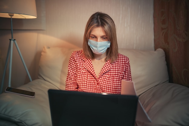 Jeune femme d'affaires dans un masque de protection médical travaille à domicile à l'ordinateur pendant l'auto-isolement et la quarantaine. Épidémie de virus coronavirus, épidémie de grippe et roman Covid ncov. Rester à la maison.