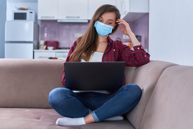 Jeune femme d'affaires dans un masque de protection médical travaille à domicile à l'ordinateur pendant l'auto-isolement et la quarantaine.