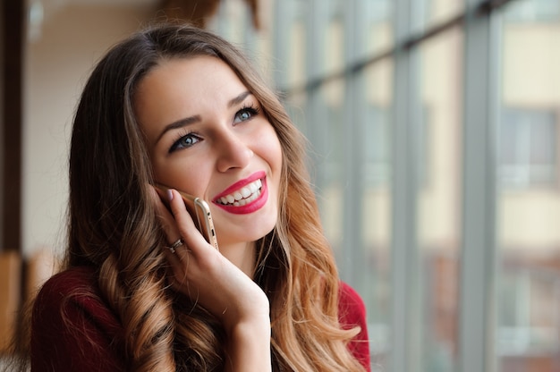 Jeune femme d'affaires dans un pull rouge avec un téléphone portable.