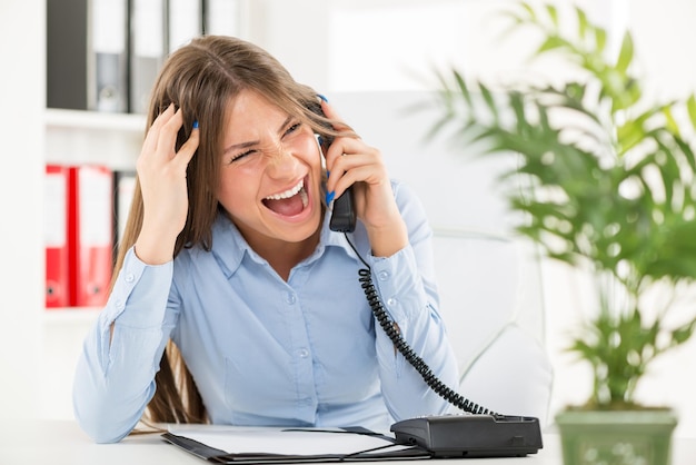 Jeune femme d'affaires dans son bureau, assise à un bureau et avec une expression de colère sur son visage criant au téléphone.