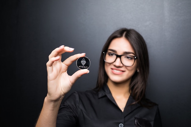 Jeune femme d'affaires dans des verres avec Litecoin en mains isolés sur un mur noir.