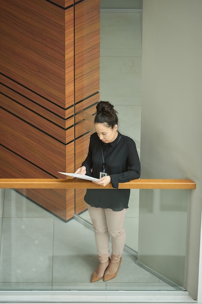 Jeune femme d'affaires debout sur le balcon et lisant un contrat commercial