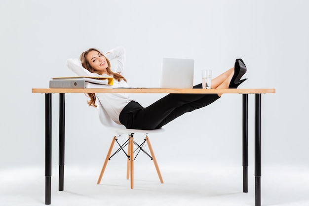 Jeune femme d'affaires décontractée assise et relaxante avec les jambes sur la table sur fond blanc