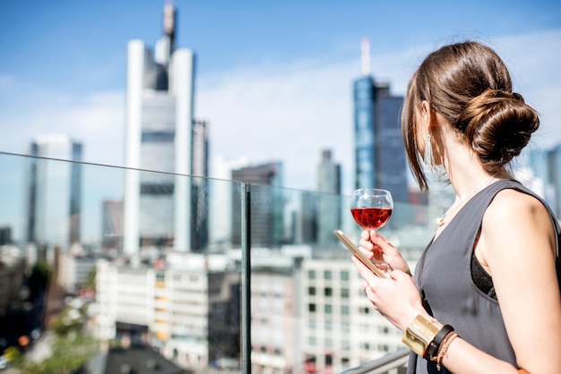 Jeune femme d'affaires dégustant du vin sur la terrasse avec une vue magnifique sur les gratte-ciel de la ville de Francfort