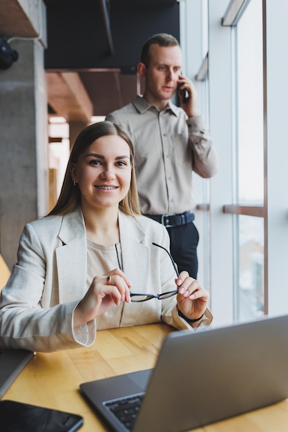 Jeune femme d'affaires derrière un ordinateur portable portant des lunettes assis à une table ayant une réunion d'affaires d'entreprise avec des collègues dans un bureau moderne Concept de carrière commerciale Mise au point sélective de l'espace libre