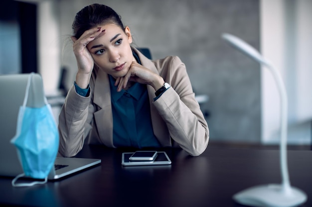 Jeune femme d'affaires désemparée pensant à quelque chose à son bureau pendant la pandémie de COVID19