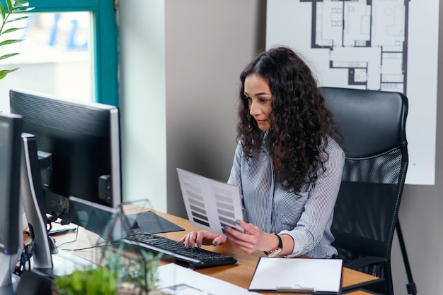 Photo jeune femme d'affaires détient la palette de couleurs et travaille à l'ordinateur dans le bureau moderne.