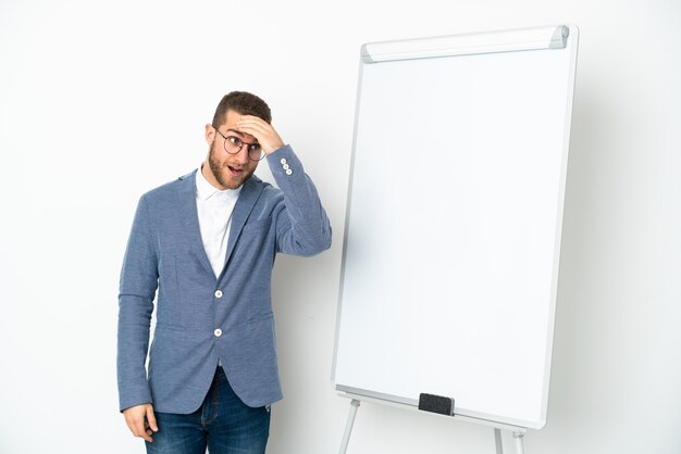 Jeune femme d'affaires donnant une présentation sur tableau blanc isolé sur fond blanc faisant un geste de surprise tout en regardant sur le côté