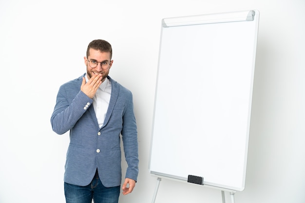 Jeune femme d'affaires donnant une présentation sur tableau blanc isolé sur un mur blanc heureux et souriant couvrant la bouche avec la main