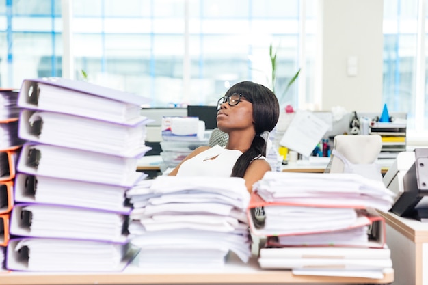 Jeune femme d'affaires dormant au bureau avec de nombreux travaux